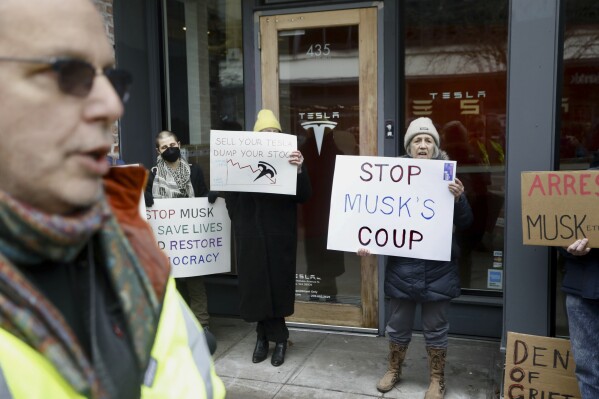 People protesting Elon Musk's actions in the Trump administration hold signs outside a Tesla showroom in Seattle on Thursday, Feb. 13, 2025. (AP Photo/Manuel Valdes)